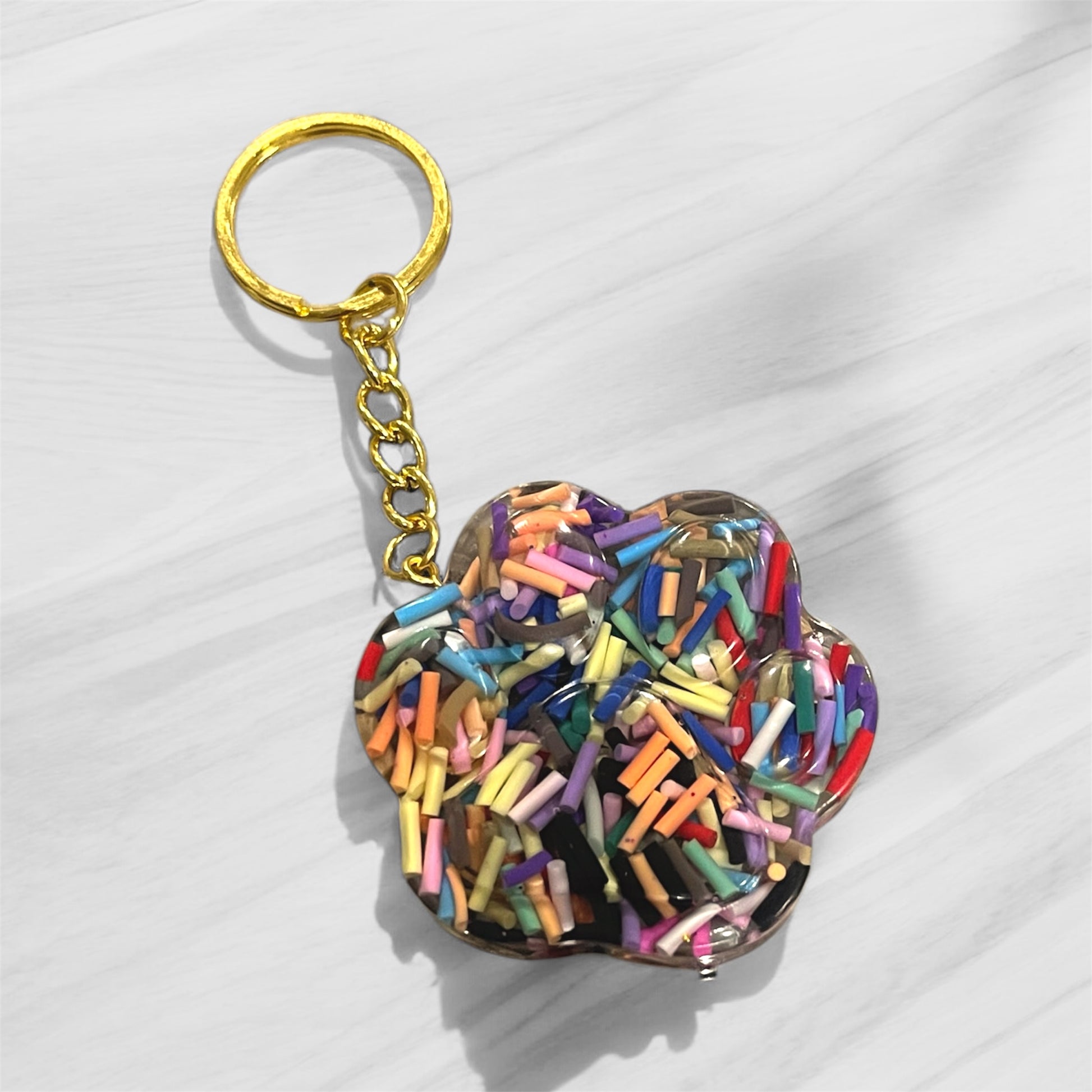 Handmade dog paw print keychain with rainbow sprinkle confetti in clear resin, featuring gold-tone hardware, perfect for pet parents and dog lovers