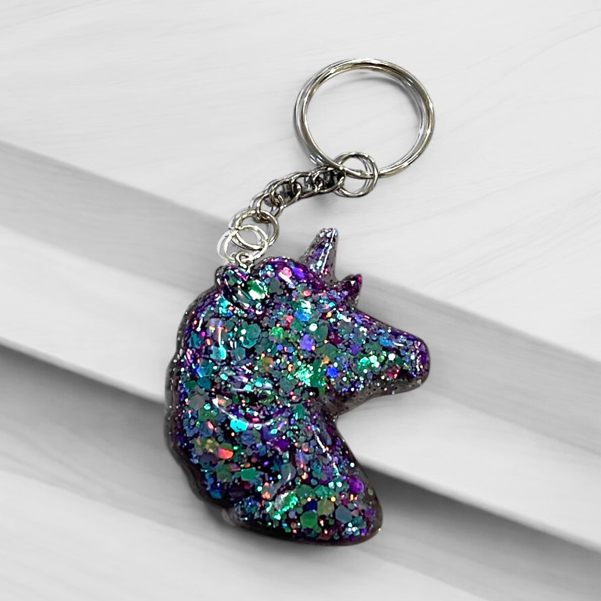 Handmade unicorn resin keychain with holographic glitter in teal, purple, and iridescent colors, featuring a mystical silhouette design and silver chain