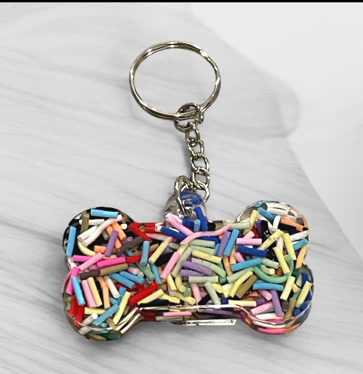 Handmade pet memorial dog bone keychain with rainbow sprinkles in crystal clear resin, perfect for pet lovers and dog moms